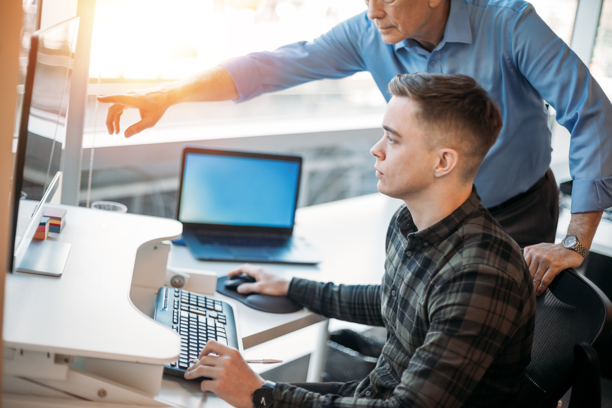 Colleague mentoring younger associate in business office while pointing at data on computer monitor