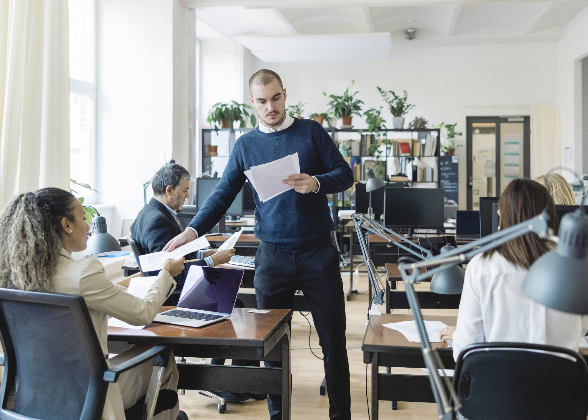 Man giving handouts to diverse employees in open plan office