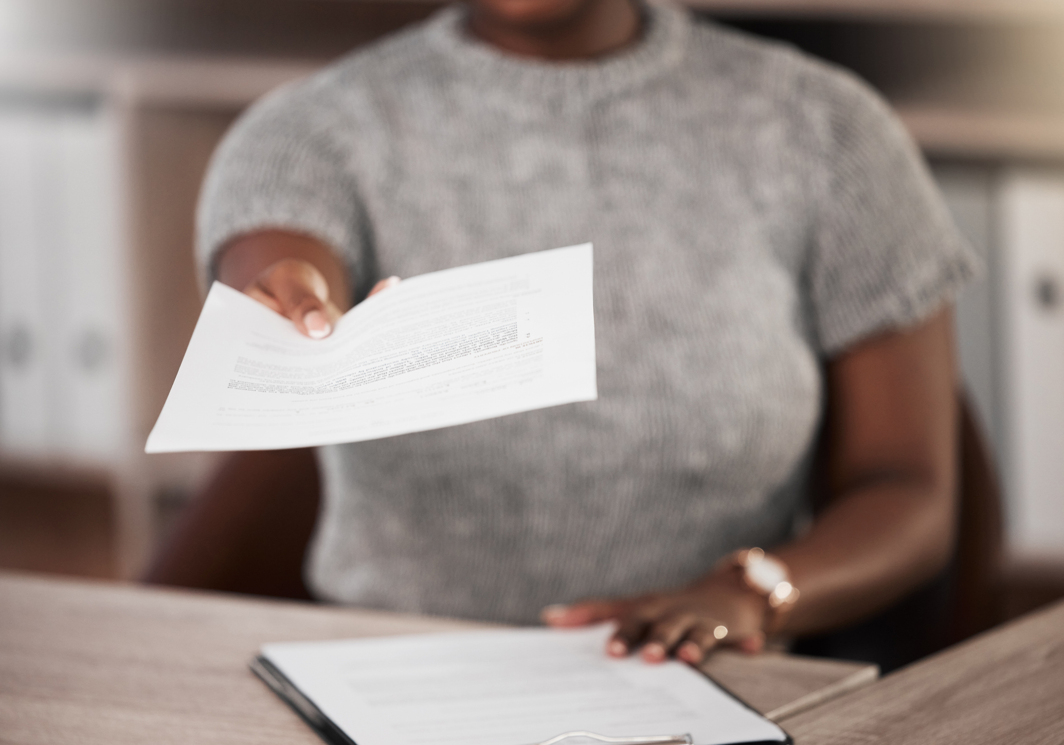 Shot of an unrecognisable businesswoman handing a document at her desk in a modern office