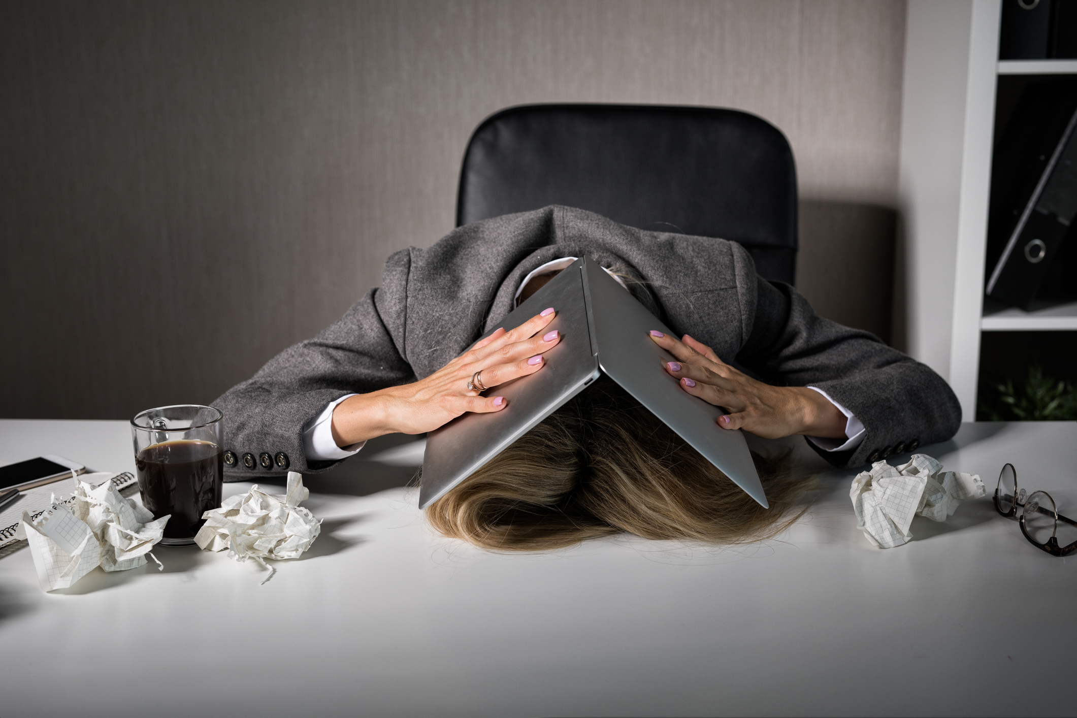 Frustrated woman hiding under laptop in office