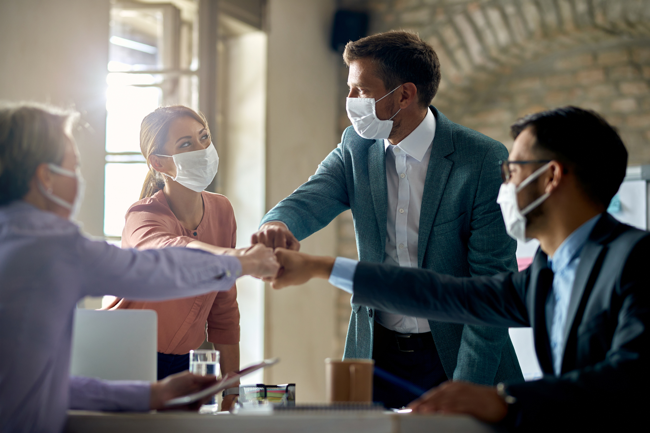 United business team with face masks colliding their fists on a meeting in the office.