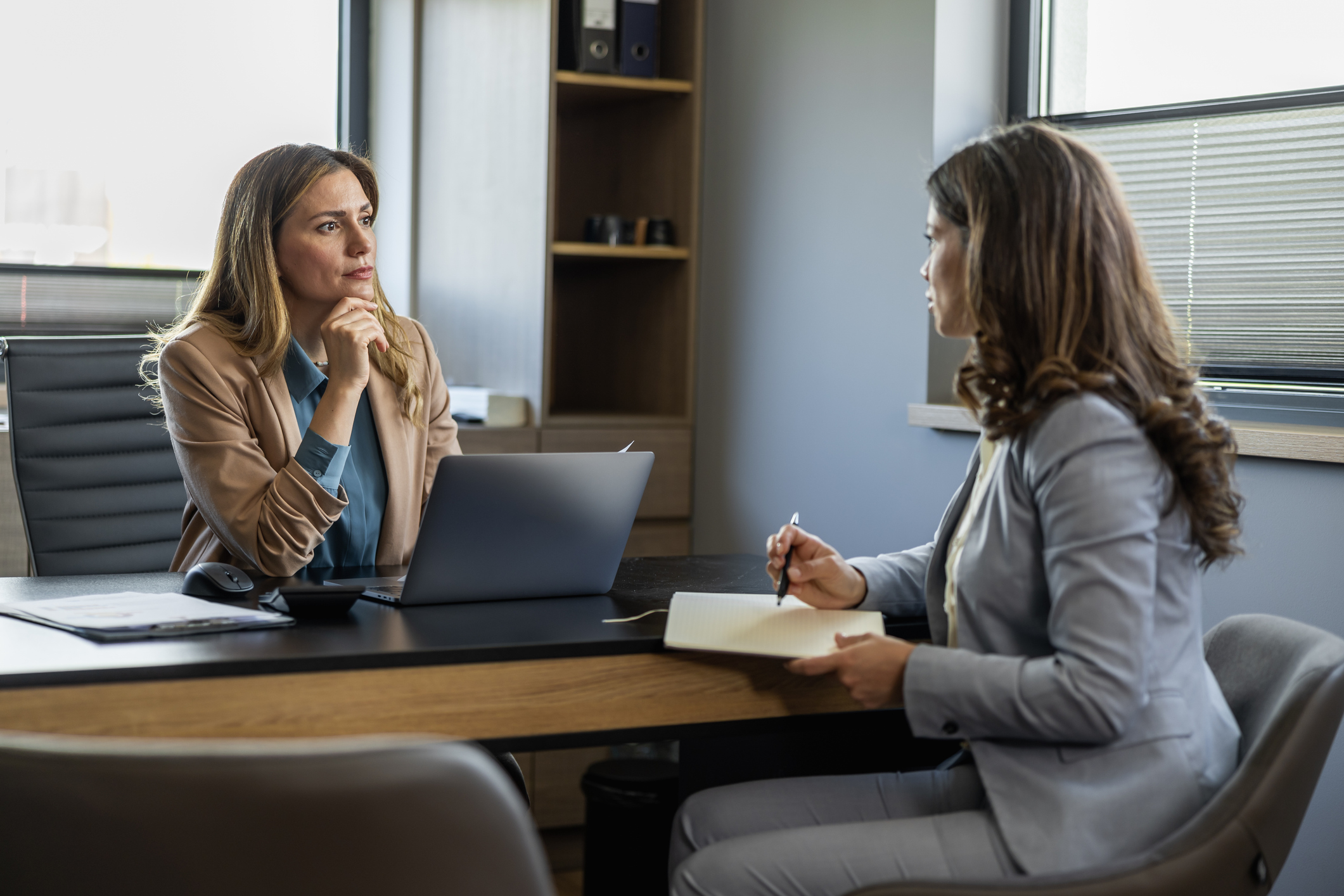 Female travel agent looking at her client, communicating with her in office and showing tours