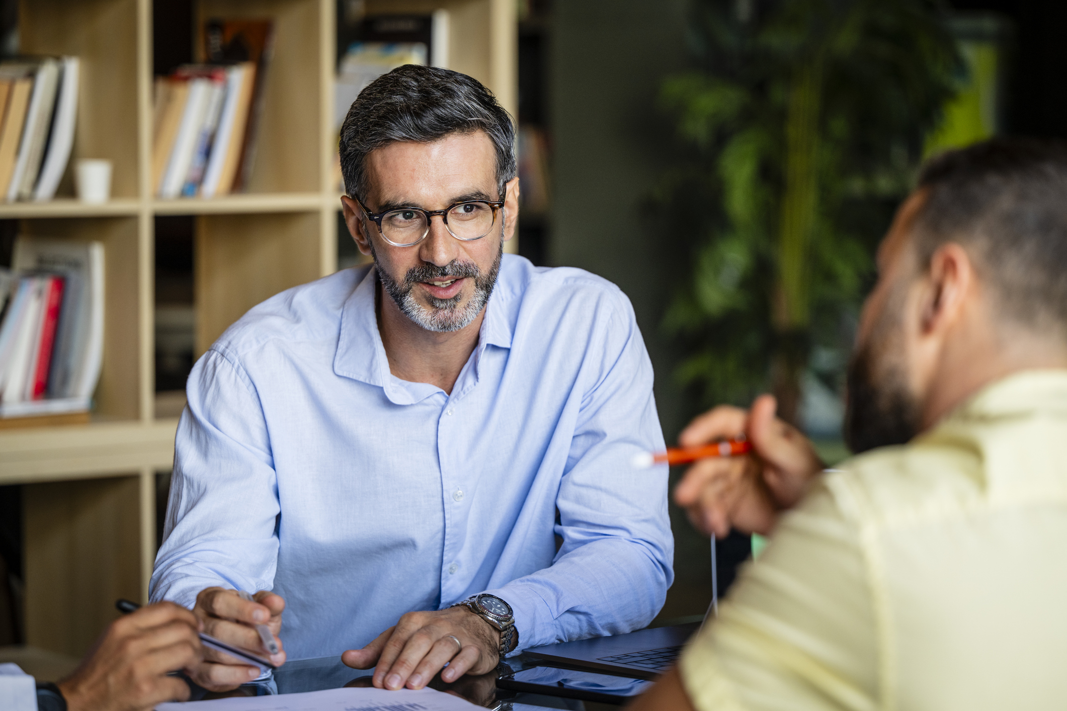 Mid adult businessman with beard and glasses, wearing blue shirt, listening and concentrating in meeting